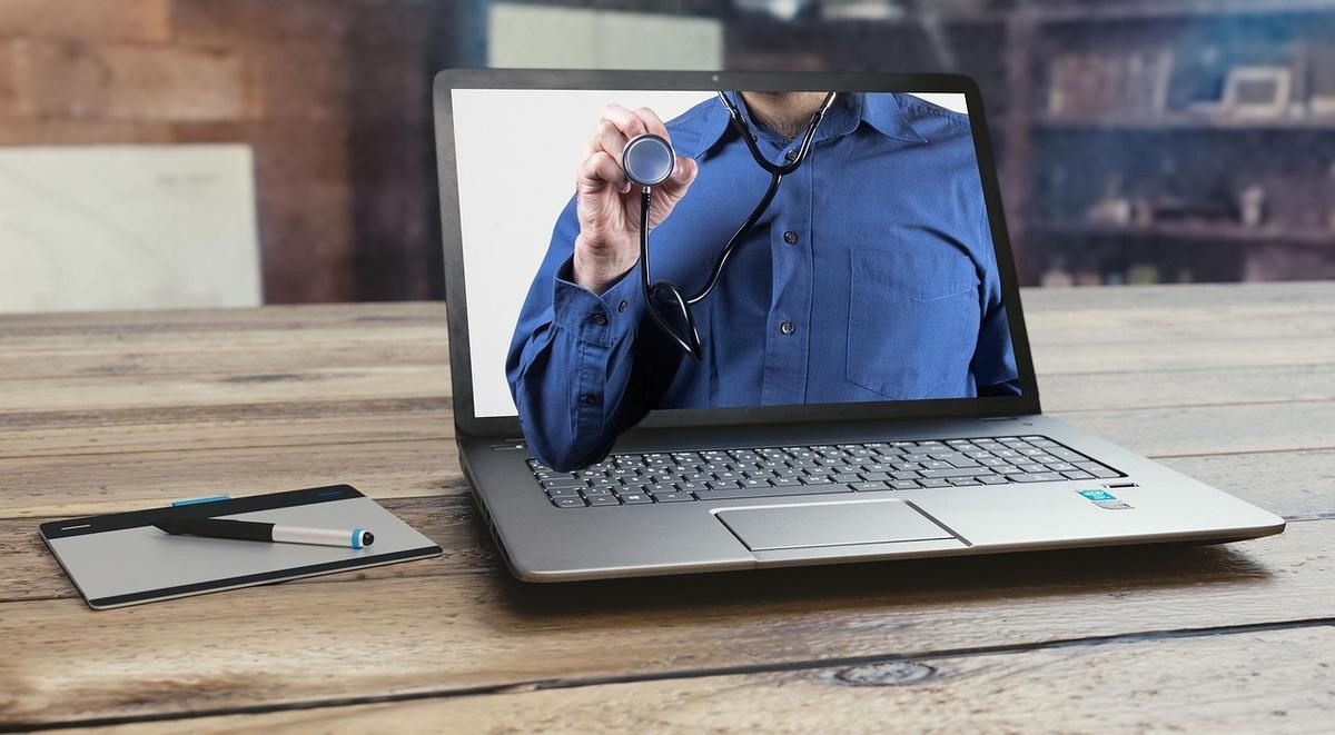 Laptop affichant une personne portant un stéthoscope, avec un stylo et un bloc-notes à proximité Laptop affichant une personne portant un stéthoscope, avec un stylo et un bloc-notes à proximité