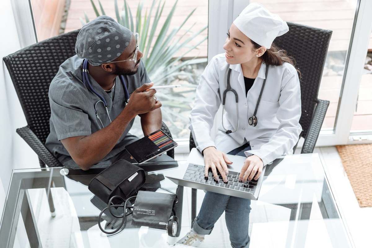 Professionnels de santé en conversation avec ordinateurs et stéthoscopes sur une table en verre Professionnels de santé en conversation avec ordinateurs et stéthoscopes sur une table en verre