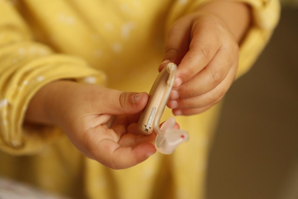 Des mains d'enfant tiennent un appareil auditif et son embout