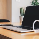 Un bureau avec ordinateur, tasse, téléphone et cactus en arrière-plan