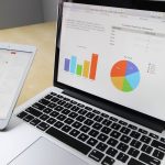 Une main tient une tablette à côté d'un ordinateur affichant des graphiques