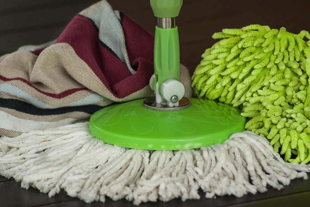 Un balai à microfibre vert avec chiffon et lingettes sur sol sombre